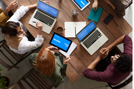 A group of diverse individuals seated around a table, each using a laptop for collaborative work.