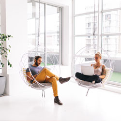 Two people sitting together in a hanging chair, using a laptop for work or leisure.